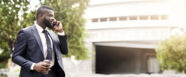 Mobil iletişim. Zarif takım elbiseli, kendine güvenen Afro-Amerikan bir adam iş görüşmesi yapıyor, fotokopi alanı ile yan görüş.