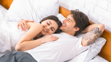 Genç bir çift yatakta birlikte yatıyor, ikisi de gülümsüyor ve görünüşe göre birlikte eğleniyorlar. Kadın erkek tarafının içine yerleşmiş, başı göğsünde dinleniyor, ve adam kolunu kadının omzuna atmış..