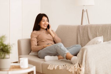 Kanepede oturan bir kadın, telefonda konuşurken rahatlamış ve gülümsüyor..