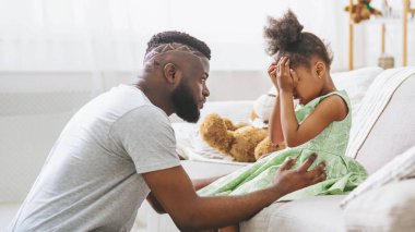 Kara baba, ağlayarak yüzünü elleriyle örten küçük kızının yanında bir kanepede diz çöküyor. Karnında rahatlatıcı bir eliyle ona uzanıyor..