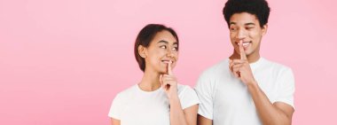 Its our secret. Teens holding fingers on lips and looking at each other, pink studio background clipart