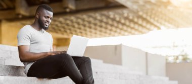 Onun laptop kodlama ve şehir wifi açık, panorama, kopyalama alanı kullanarak Gülümseyen Afrikalı Amerikalı adam