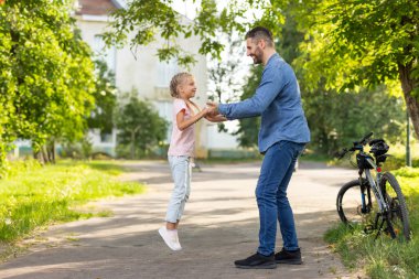 Bir baba ve kızı güneşli bir günde banliyöde birlikte oynuyorlar. Kız havada zıplarken, babası ona gülümsüyor..