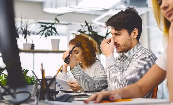 stock image Tired and overworked manager sitting in front of computer and trying to concentrate, his eyes are dry and hurt, panorama