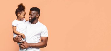 Afro-Amerikalı bir baba gülümseyip şeftali renkli bir arka plana karşı küçük kızını kollarına alır. Her ikisi de birbirlerine bakıp gülüyor ve uzayı kopyalıyorlar.