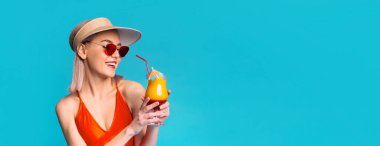 Bu resim kırmızı mayo ve güneş gözlüğü takan genç bir kadını gösteriyor. O, pipetle bir kokteyl tutuyor. Kadının yüzünde mutlu bir ifade var. Arkaplan koyu mavi, kopyalama alanı