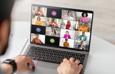 İşadamı birden fazla meslektaşıyla bir video konferans toplantısına katılmak için bir dizüstü bilgisayar kullanıyor. Dizüstü bilgisayar ekranı, her katılımcının yüzlerini gösteren bir görüntü kaynağı ızgarası görüntüler