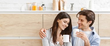 Genç bir çift modern bir mutfakta bir fincan kahvenin tadını çıkarıyor. Kadın gülümseyen adama bakarken, adam ona sevgi dolu bir ifadeyle bakıyor, boşluğu kopyalayarak.