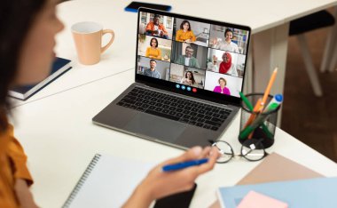 Bu görüntü, bir kadının dizüstü bilgisayarında bir video konferans toplantısına katıldığını gösteriyor. Ekranda birden fazla katılımcı ızgara biçiminde görüntülenir, bu da sanal bir takım toplantısı veya