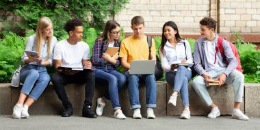 Öğrencilerin hayatı. Üniversite kampüsünde kitap ve cihazlarla oturan, derslere hazırlanan arkadaşlar
