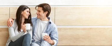 Genç bir çift mutfakta yan yana oturup kahve fincanlarını tutarak birbirlerine sevgiyle bakıyorlar..