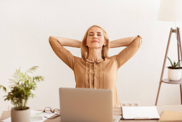 Freelance Woman Resting After Work, Holding Arms Behind Head