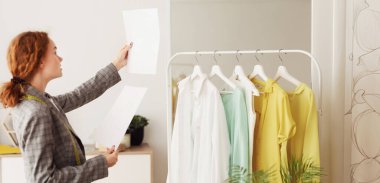 Genç tasarımcı kontrol ve kağıtlar üzerinde çizimler karşılaştırarak, terzi Studio çalışma