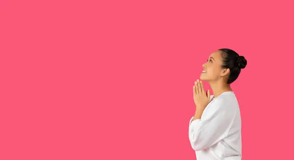 Stock image Asian woman with her hands clasped together in prayer looks upward with a hopeful expression. Her dark hair is pulled back in a bun, and she is wearing a white blouse, copy space