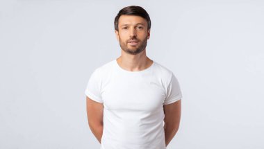 Beyaz stüdyo arka planda kameraya bakarak elleri arkasında duran ciddi bir adam. İzole, Boş Alan