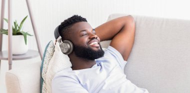 Sakallı siyah bir adam koltukta oturuyor, rahat bir ifadeyle arkasına yaslanıyor. O, kulaklık takıyor ve müzik dinliyor. Yüzünde kocaman bir gülümseme var.