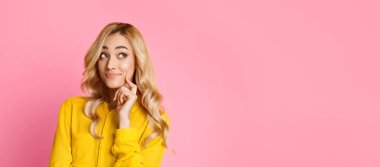 Bu resim, sarı gömlek giyen uzun sarı saçlı genç bir kadını gösteriyor. Pembe bir arka planın önünde duruyor ve düşünceli bir görünüm sergiliyor..