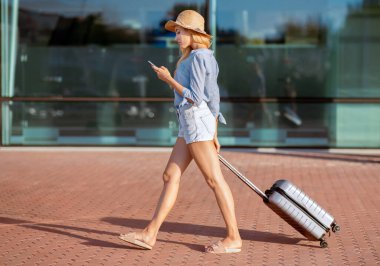 Seyahatte gideceğimiz yeri ya da oteli bulmak için GPS kullanan bagajlı bir kadın gezgin, cep telefonu haritası uygulaması ile geziniyor