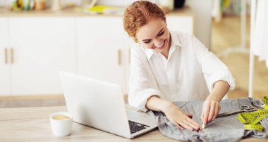 Bir kadın tebeşirle kumaşı işaretlerken gülümsüyor, evinde bir laptop ve bir fincan kahveyle bir masada oturuyor..