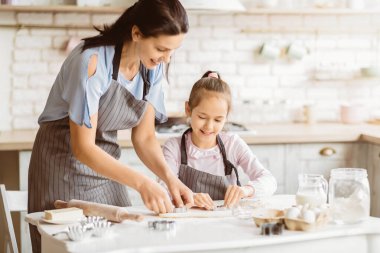 Bir anne ve kızı mutfaklarında birlikte kurabiye pişiriyorlar. Kurabiye kesiciyle kurabiye hamurunun şekillerini keserken anne kızına rehberlik ediyor..