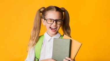 Kamera önünde göz kırpan komik ilkokul kızı. Stüdyoda sarı arka planda poz veren kitapları tutuyor. Okula Dönüşün kutlu olsun.