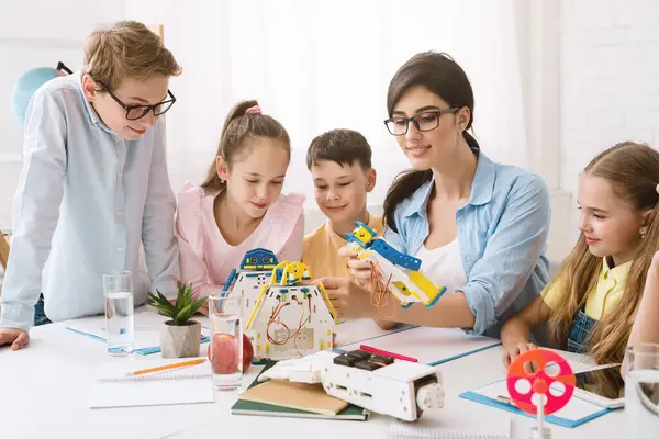 stock image A group of young students are engaged in a STEM class, working together to build a robot. A teacher guides them, while they follow instructions and use their creativity to solve problems.