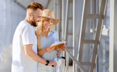 Yolculuk için hazır olun. Gülen eşler pasaportlarını ve biletlerini havaalanı penceresinde tutuyorlar.