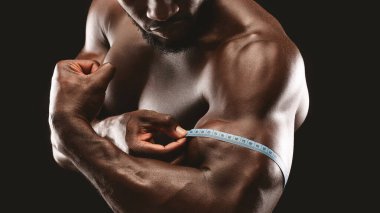 Kaslı bir adam kaslarını mezurayla ölçer. Fiziğini ve uygunluğunu gösterir..