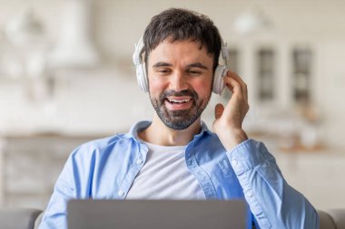 Evindeki koltukta oturan bir adam, kulaklık takıyor ve dizüstü bilgisayarını kullanırken gülümsüyor. Müzik ya da ses kaydı dinliyor gibi görünüyor..
