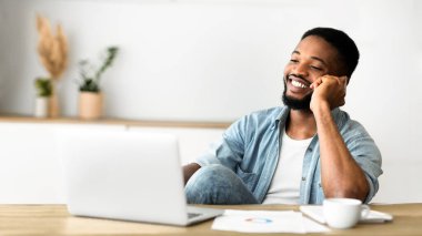 Handsome black man talking on phone while sitting at workplace in office