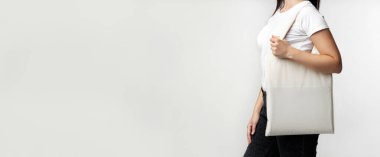 Beyaz gömlekli ve siyah pantolonlu bir kadın beyaz arka planda beyaz bir çanta tutuyor..