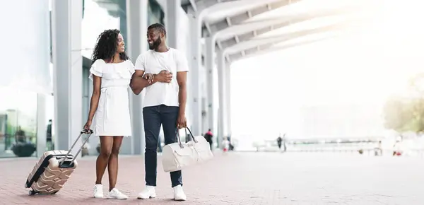 stock image A young black couple, dressed in casual white clothing, walks through a modern airport terminal. They are smiling and looking at each other, suggesting a fun vacation ahead, copy space