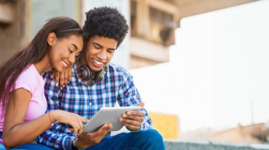 Genç bir Afro-Amerikan çift bir dizi basamağa oturup birlikte bir tablete bakıyorlar. Kız, kolunu omzuna atmış adamın solunda oturuyor. İkisinin de yüzünde gülümseme var.