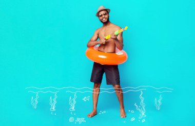 Su tabancası ve şişme yüzüklü neşeli siyah adam mavi stüdyo arka planında poz veriyor, yaz tatilinin tadını çıkarıyor.