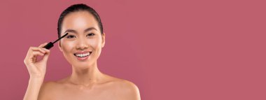 Neşeli, üstsüz, maskeli, kameraya gülümseyen, gözlerine makyaj malzemesi süren, mor stüdyo arka planında yeni makyaj ürünlerinin keyfini çıkaran, yakın plan, uzay kopyası