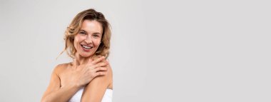 Natural Beauty. Portrait Of Attractive Middle Aged Woman Wrapped In Bath Towel Smiling At Camera, Happy Beautiful Good Looking Lady Enjoying Selfcare, Posing Over Light Studio Background, Copy Space