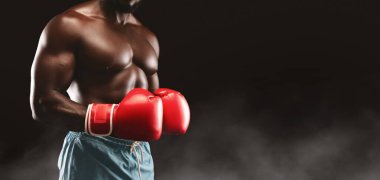 A shirtless boxer wearing red boxing gloves stands in a fighting stance against a black background with smoke. clipart