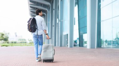 Erkek gezgin havaalanına geldi, valiz ve sırt çantasıyla dışarı çıktı, girmek için doğru terminali arıyor.