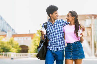 Genç siyah bir çift, şehir caddesinde yan yana yürüyor. Kolları kızların omzuna dolanmış bir adam. İkisi de gülümsüyor ve birbirlerine bakıyorlar, içkilerini ellerinde tutuyorlar, boşluğu kopyalıyorlar.