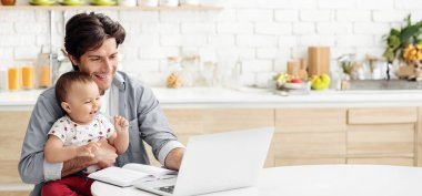 Bir baba mutfaktaki bir masada oturuyor, dizüstü bilgisayarla çalışırken bebeğini kollarında tutuyor. Bebek gülümsüyor ve babaya bakıyor, baba ise işine odaklanmış, kopya.