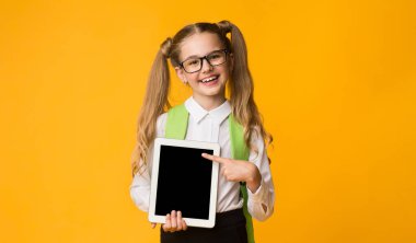 E-öğrenme. Dijital tabletli ilkokul öğrencisi kız. Sarı Stüdyo Arkaplan 'da boş bilgisayar pozu veriyor. Model