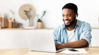 Bir adam içeride laptopuyla çalışırken gülümsüyor..