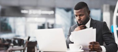 Ciddi bir siyahi iş adamı laptopta çalışıyor. Açık kafede oturan evrakları tutuyor. İş Kariyeri Konsepti