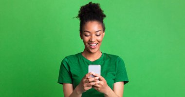 Harika bir uygulama. Yeşil stüdyo duvarında akıllı telefon kullanan mutlu zenci kadın portresi