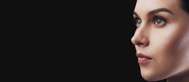 Karanlık bir arka planda bir kadın profilinin yakın plan çekimi. O ciddi bir ifadeyle yana bakıyor..