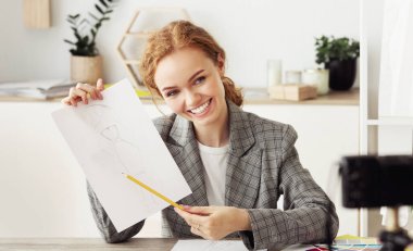 Vlog için video yapıyorum. Mutlu stil tasarımcısı çizimini kameraya gösteriyor, evde çalışıyor, boşluğu kopyalıyor.