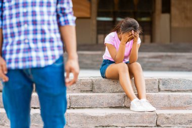 Ekose gömlekli ve kot pantolonlu bir adam ondan uzaklaşırken, genç bir kız elleri havada beton merdivenlerde oturuyor. Üzgün ya da ağlıyor gibi görünüyor..