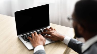Boş ekranlı dizüstü bilgisayarda yazan, ofiste çalışan siyahi işadamının konsantresi. Omuz dansı
