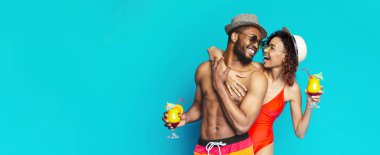 Mayo giymiş Afro-Amerikalı bir çift, şapka takan bir adam ve kırmızı mayo giyen bir kadın, gülüyorlar ve ellerinde kokteyller tutuyorlar.