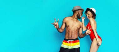 Yaz kıyafetleri içinde genç bir siyah çift parlak mavi bir arka plana karşı poz veriyor. İkisi de gülümsüyor ve birbirlerine eşlik etmekten zevk alıyor gibi görünüyorlar.